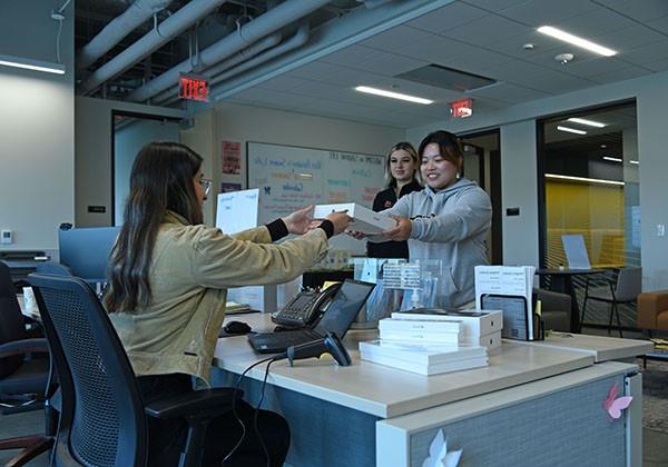 Student picking up a laptop from the front desk of a lobby.